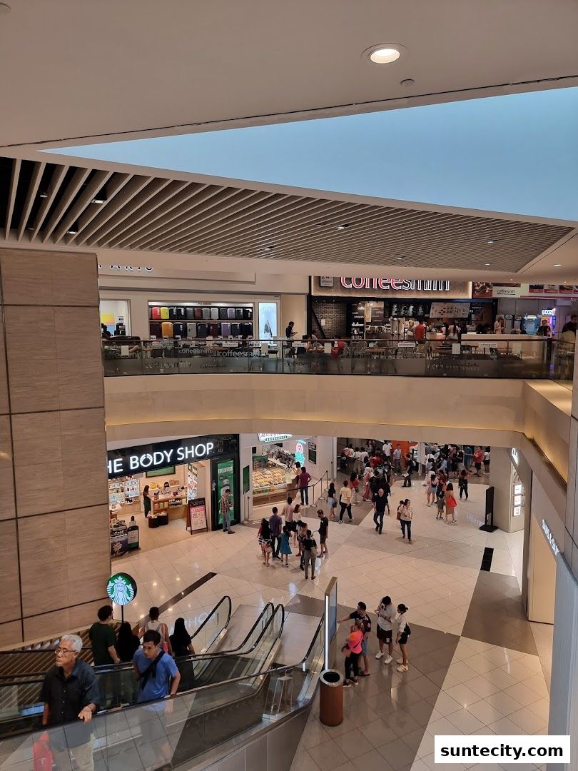 An interior view of a shopping mall with escalators and various shops, including The Body Shop.