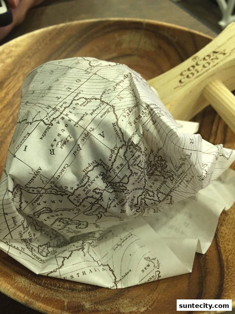 A food item wrapped in paper with a world map design, served on a wooden plate.