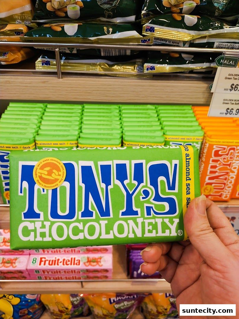 A hand holds a bar of Tony's Chocolonely chocolate in front of a shelf of chocolates.