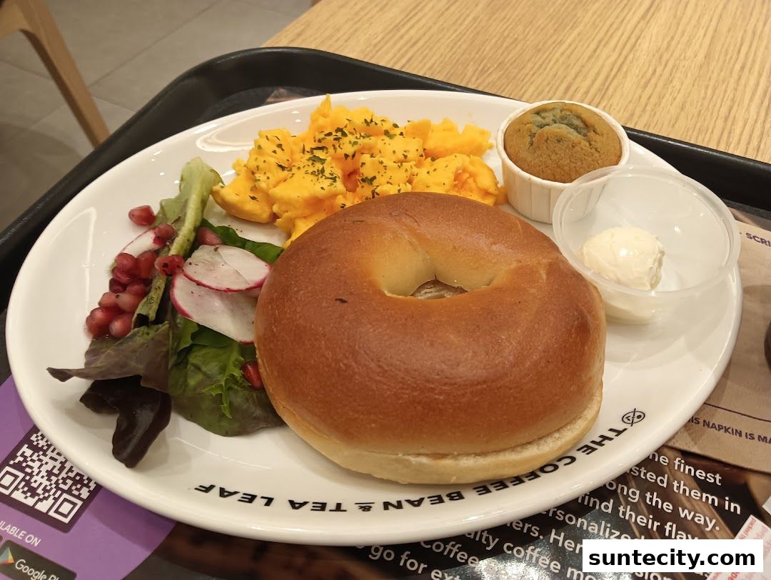 A breakfast plate with a bagel, scrambled eggs, salad, muffin, and cream cheese.