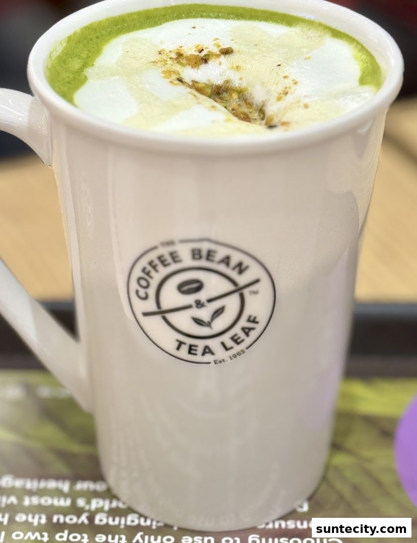 A close-up of a white mug with the Coffee Bean & Tea Leaf logo, filled with a creamy green beverage.