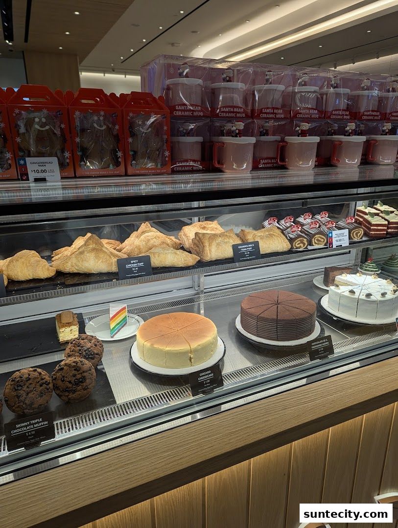 A display case filled with pastries, cakes, muffins, and holiday-themed mugs.