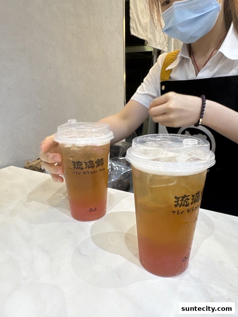 Two refreshing drinks with layered colors are presented by a staff member.