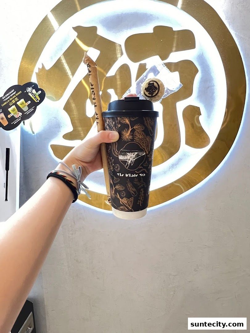 A hand holds a branded cup and straw from The Whale Tea with a cookie.