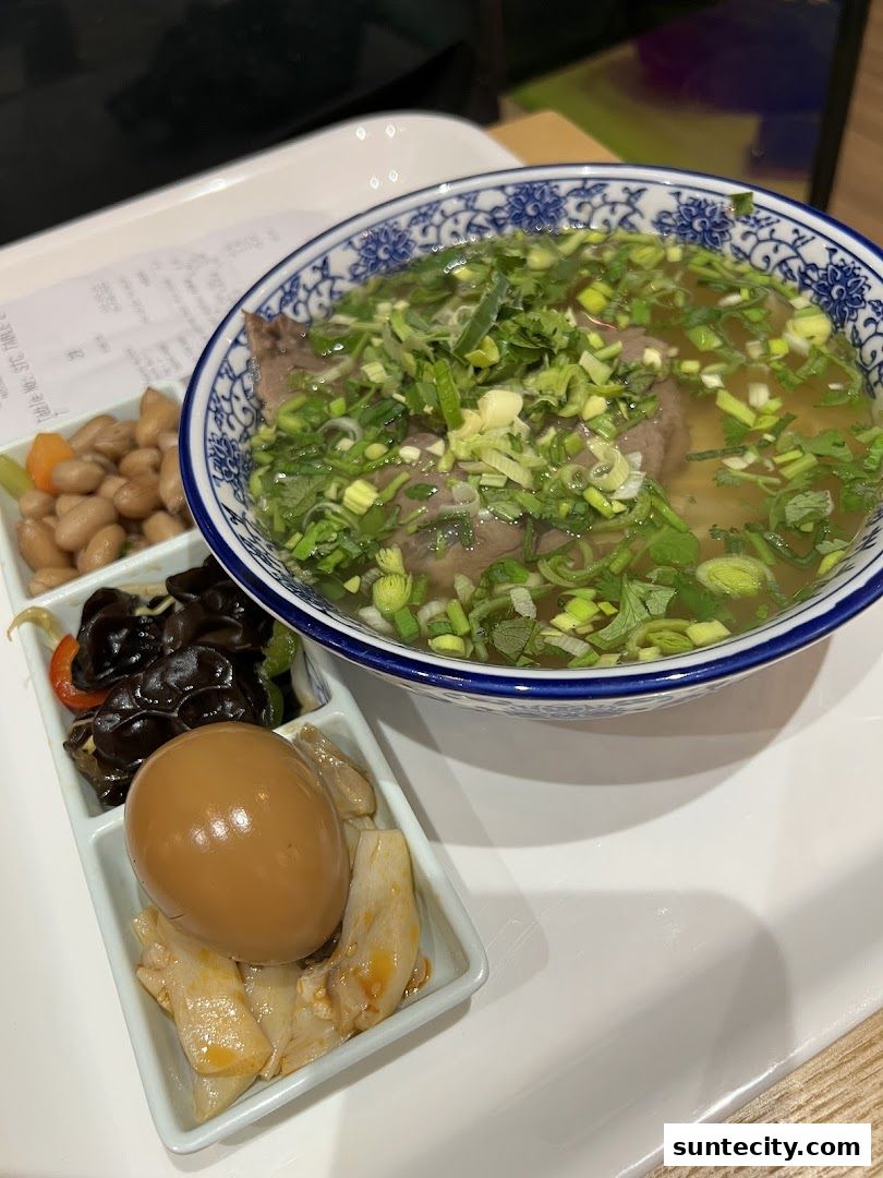 A bowl of Lanzhou beef noodles with side dishes and a receipt on a tray.