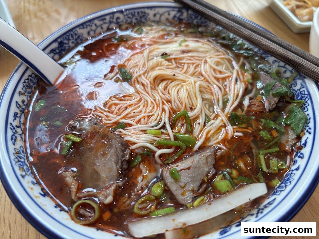 A close-up of a steaming bowl of Lanzhou beef noodles with tender beef and fresh scallions.
