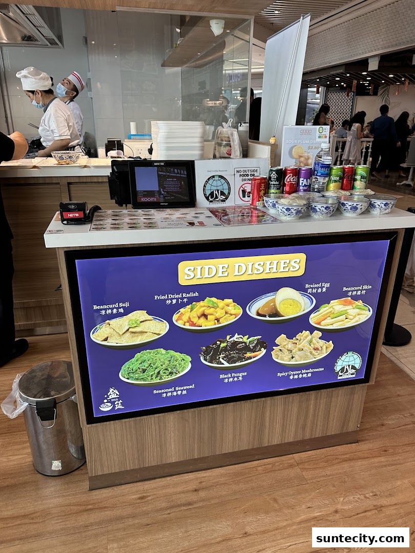 A display of various side dishes offered at a restaurant, with drinks and a trash can nearby.
