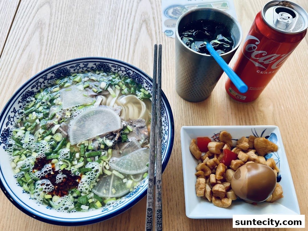 A bowl of Lanzhou beef noodles with a side of pickled vegetables and a Coca-Cola.