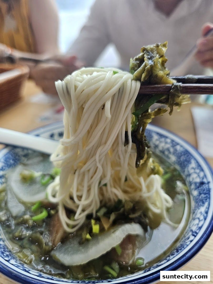 A close-up shot of Lanzhou beef noodles being lifted with chopsticks, showcasing the noodles and broth.