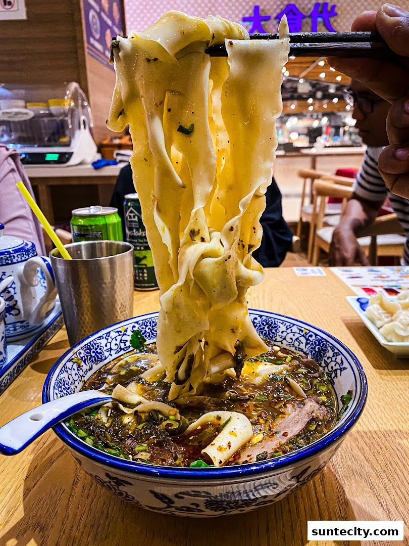 A close-up shot of a steaming bowl of Lanzhou beef noodles being lifted by chopsticks.