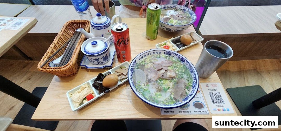 A table setting with two bowls of Lanzhou beef noodles, drinks, and side dishes.