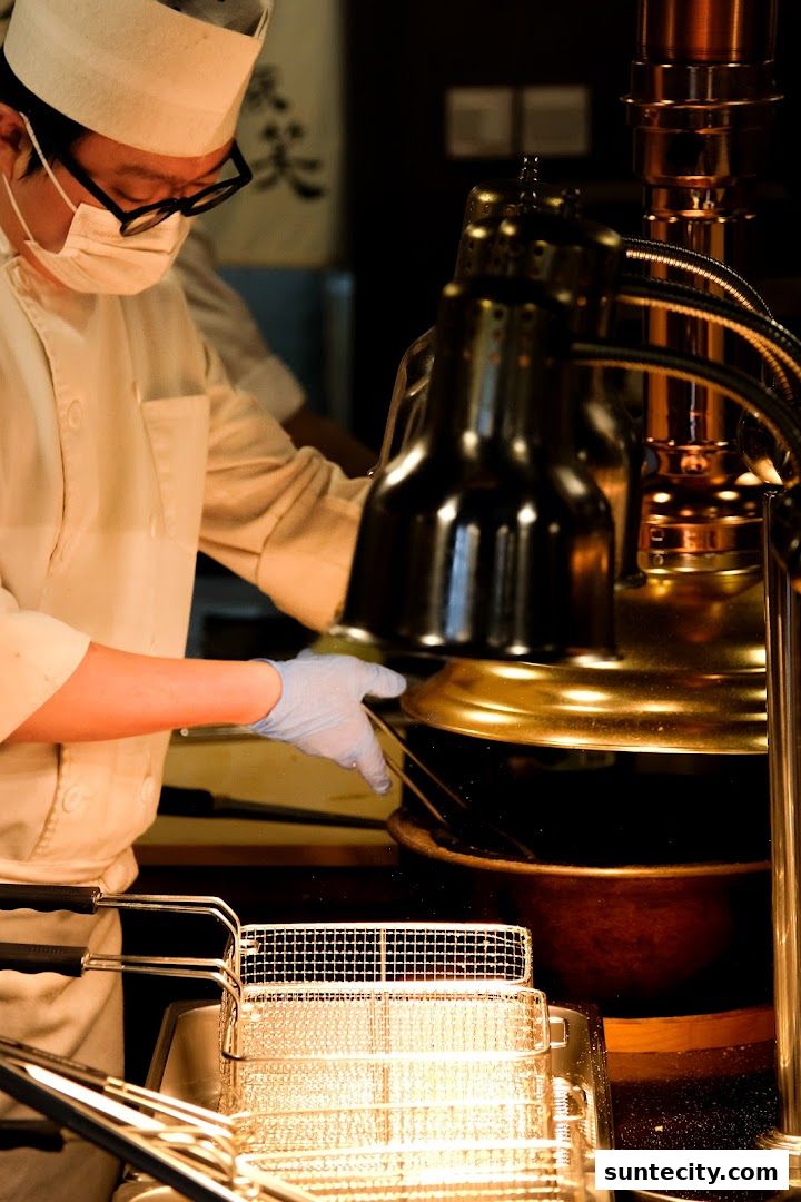A chef in uniform prepares food using a deep fryer and warming lamps.