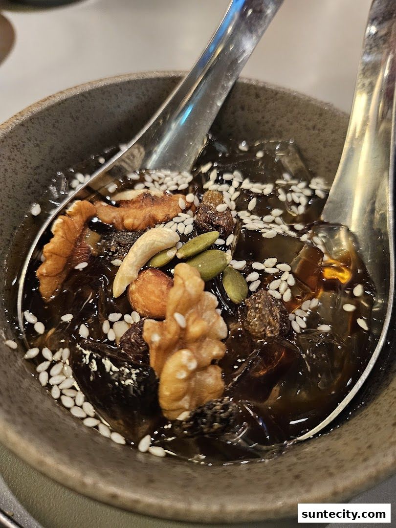 A close-up of a dessert bowl filled with jelly, nuts, seeds, and dried fruits.