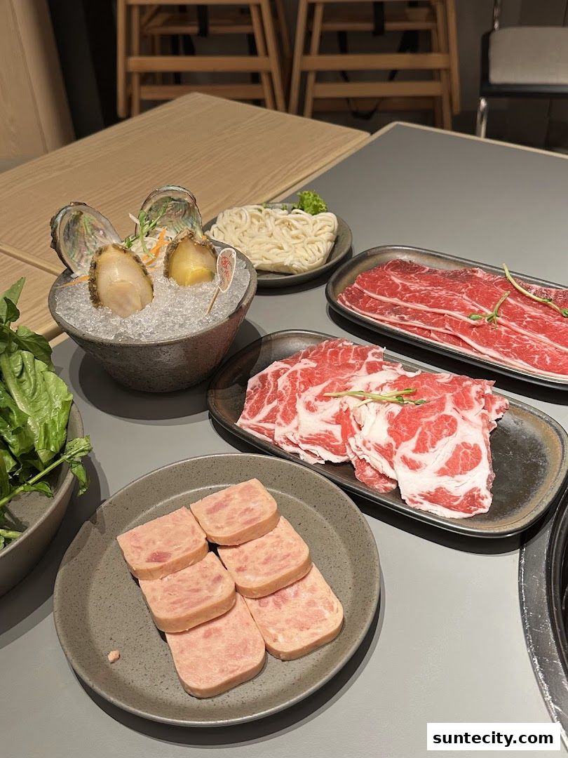 A table laden with hotpot ingredients including abalone, sliced meats, noodles, and spam.