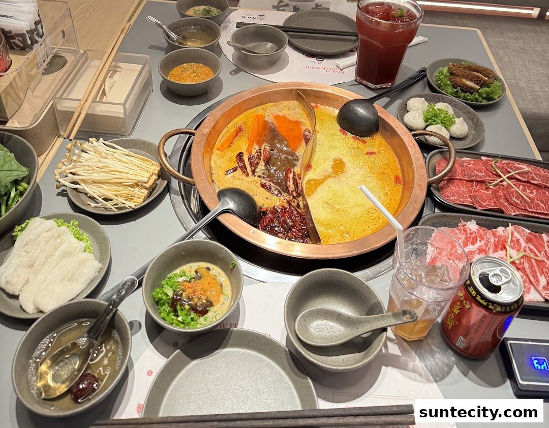 A table laden with a split hotpot, thinly sliced beef, meatballs, enoki mushrooms, and drinks.