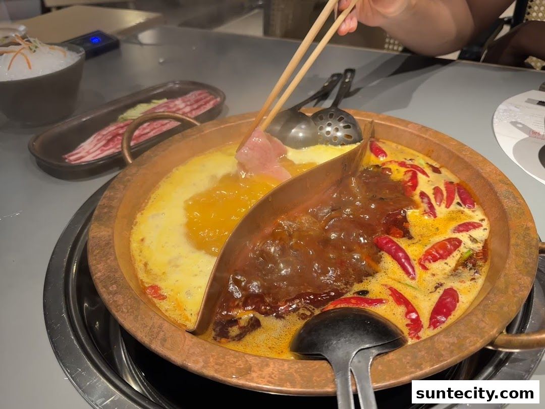 A split hot pot with creamy broth and spicy broth, with thinly sliced meat being added.