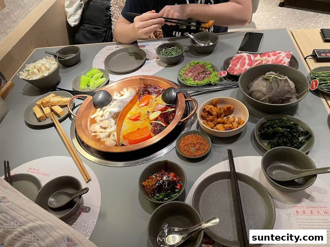 A table laden with various dishes for a hotpot meal, including meats, vegetables, and dipping sauces.