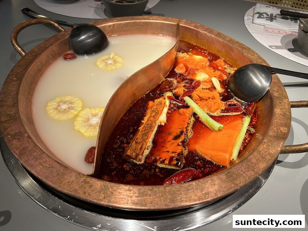 A split hot pot with creamy broth and spicy broth, featuring corn, jujubes, and ingredients like tofu and vegetables.