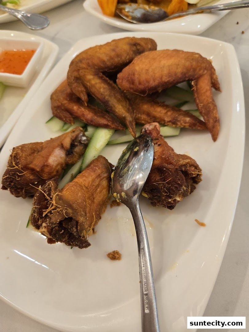A plate of crispy fried chicken wings served with cucumber slices and a side of dipping sauce.