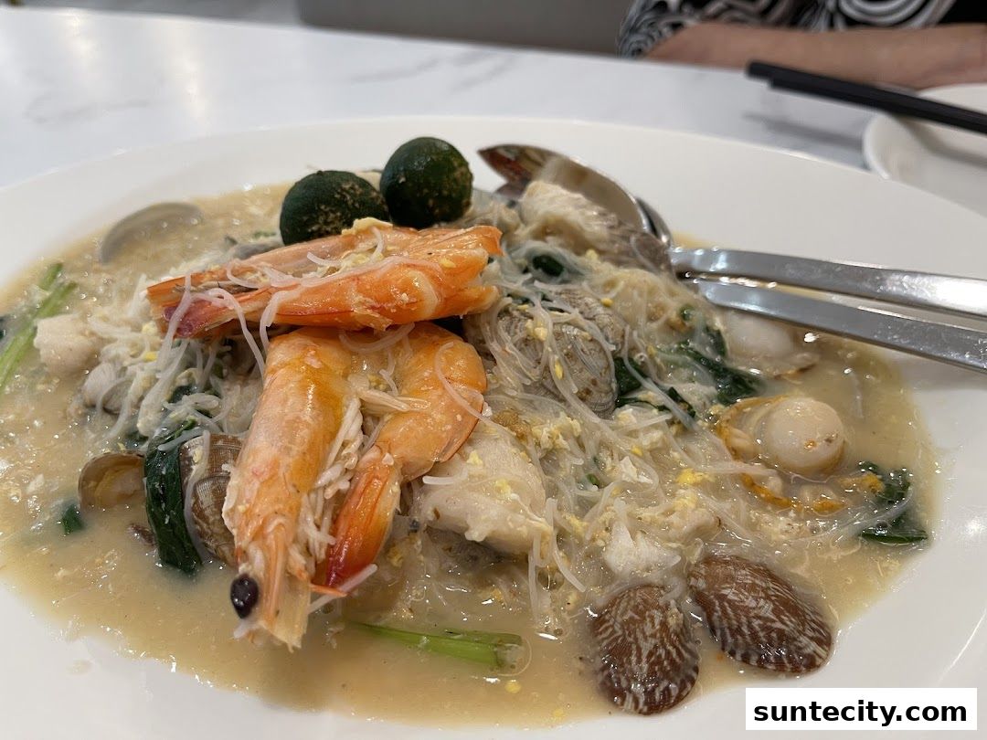 A close-up of a seafood noodle dish with prawns, clams, and scallops in a savory broth.