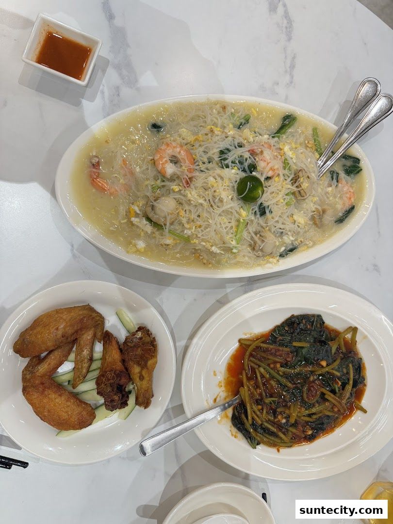 A table at White Restaurant Suntec City with three dishes: fried chicken wings, stir-fried vegetables, and a noodle dish.