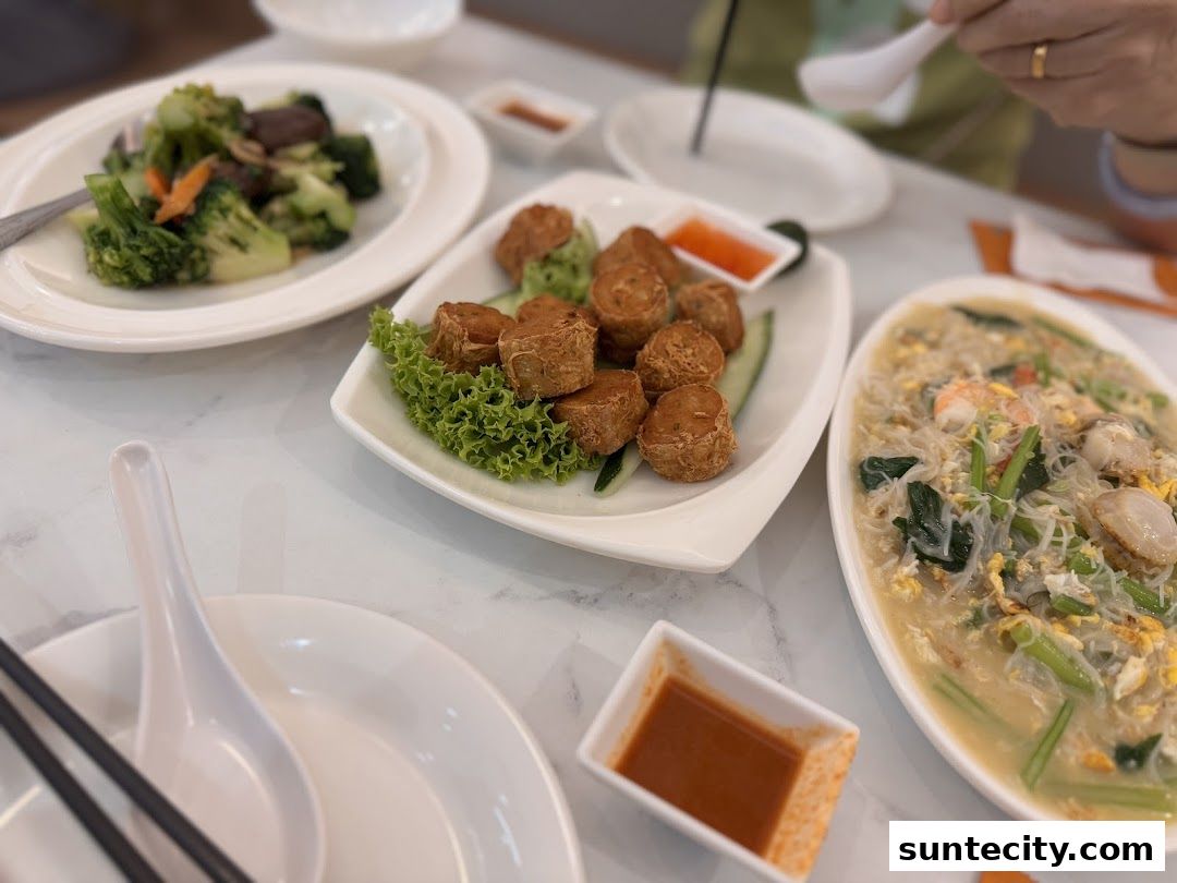 A table laden with delicious Chinese dishes, including stir-fried vegetables, fried rolls, and noodle soup.