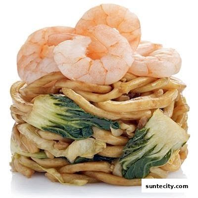 A close-up of a tower of noodles with bok choy and topped with shrimp.