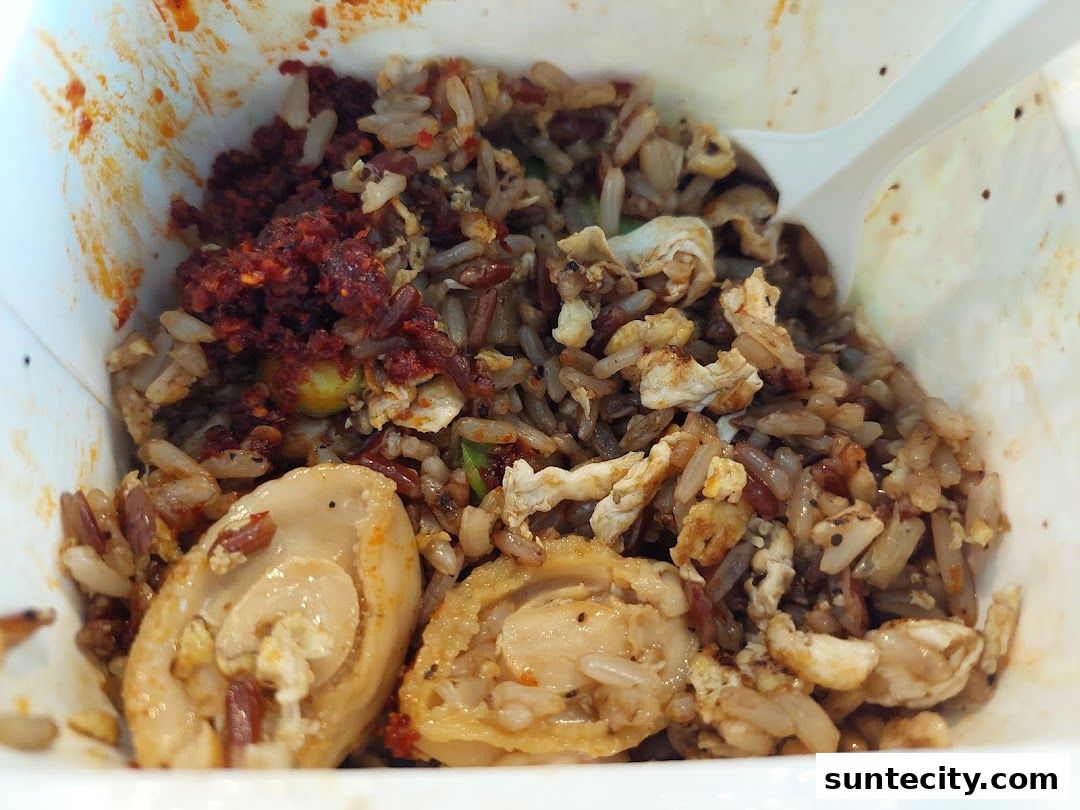 A close-up of a takeaway box filled with fried rice, chili paste, and pieces of abalone.