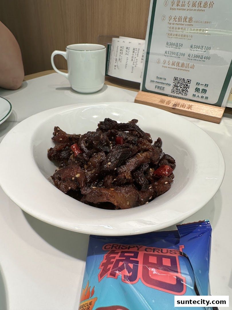 A bowl of savory Hunan cuisine dish with a cup and a snack bag on a table.