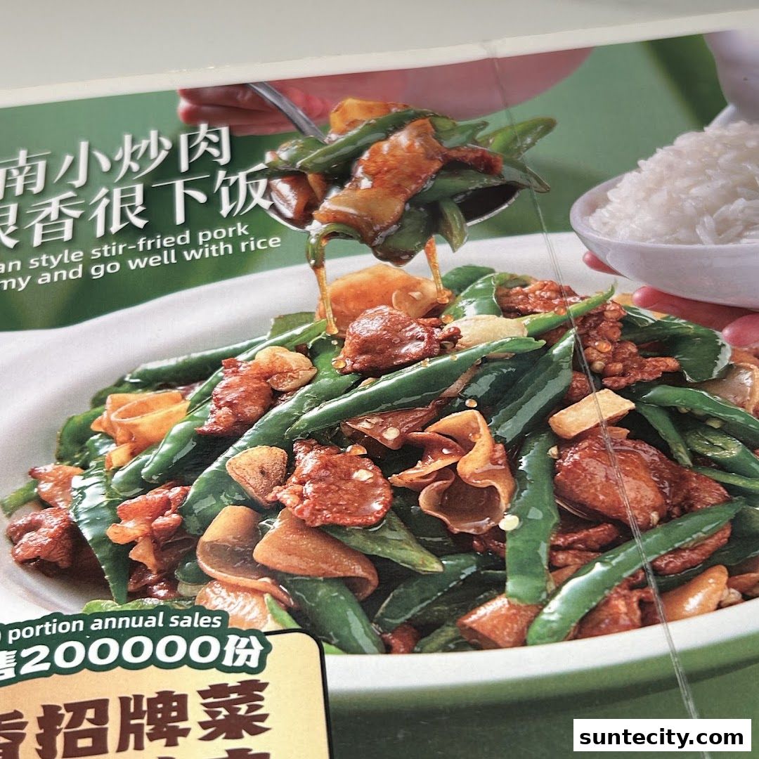 A close-up of a stir-fried dish with pork and green beans, served with rice.