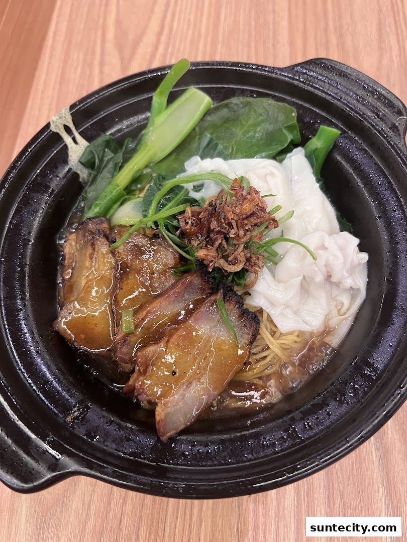 A close-up of a steaming bowl of Hong Kong-style noodles with char siu pork and wontons.