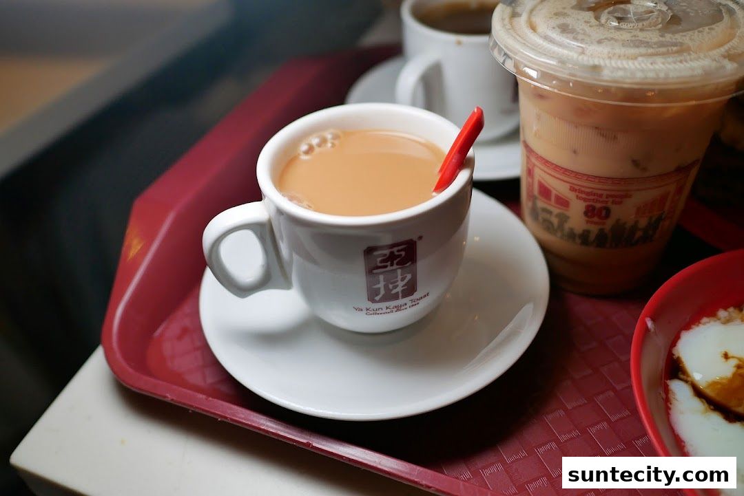 A close-up of a cup of milk tea with a red stirrer and an iced beverage on a tray.