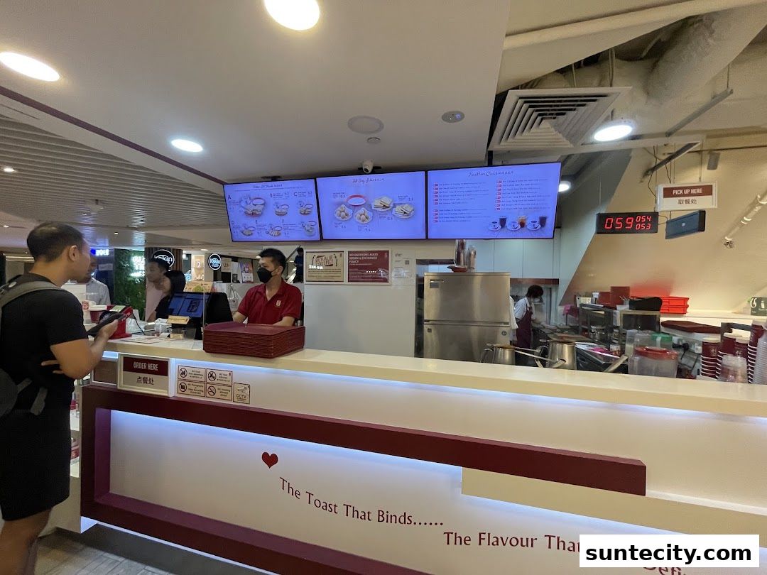 Customers ordering at the counter of Ya Kun Kaya Toast with digital menus above.