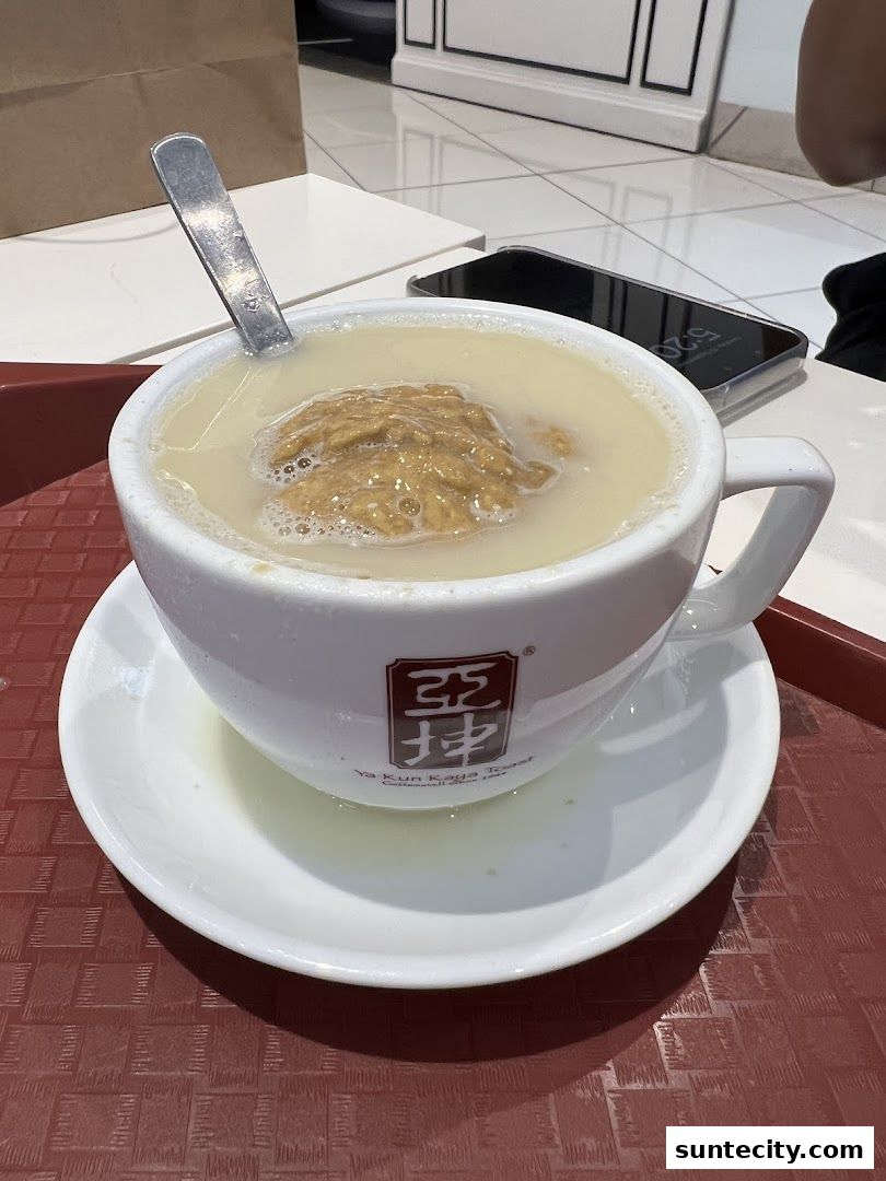 A cup of Ya Kun Kaya Toast's signature drink with a spoon and a phone on the table.
