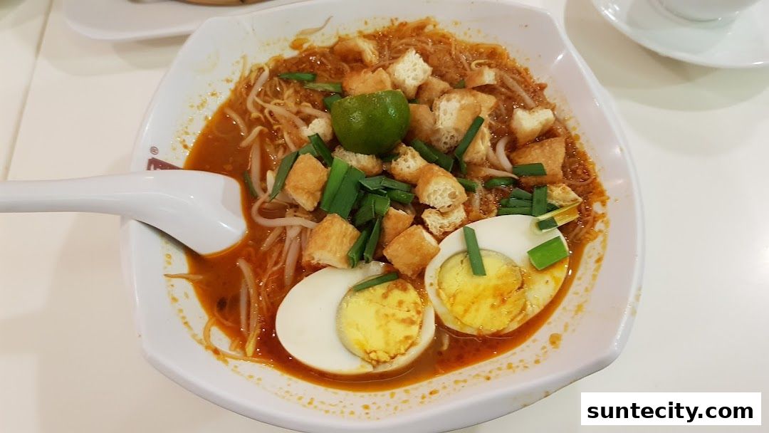 A bowl of Laksa with half-boiled eggs, bean sprouts, fried dough, and lime.