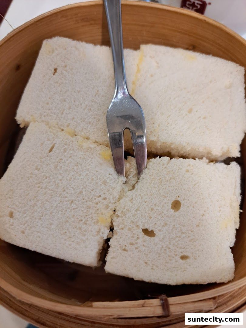 A fork is stuck in a serving of kaya toast slices in a bamboo steamer.
