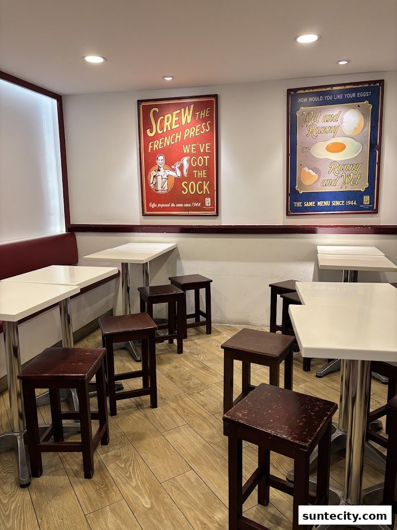 Interior of a cafe with tables, stools, and vintage-style posters on the wall.