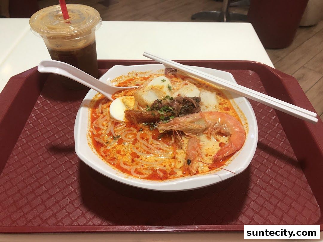 A bowl of Laksa with a prawn and a drink on a tray.