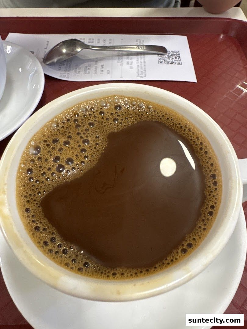 A close-up of a frothy cup of coffee with a spoon and receipt on a red tray.