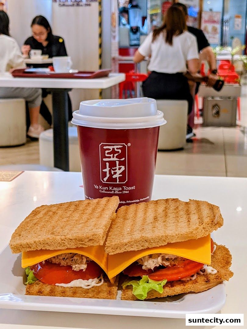 A close-up of a tuna and cheese sandwich with a cup of coffee from Ya Kun Kaya Toast.