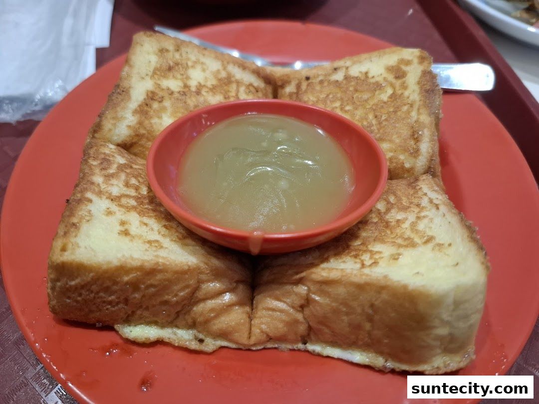 A close-up shot of golden-brown French toast served with a small bowl of kaya jam.