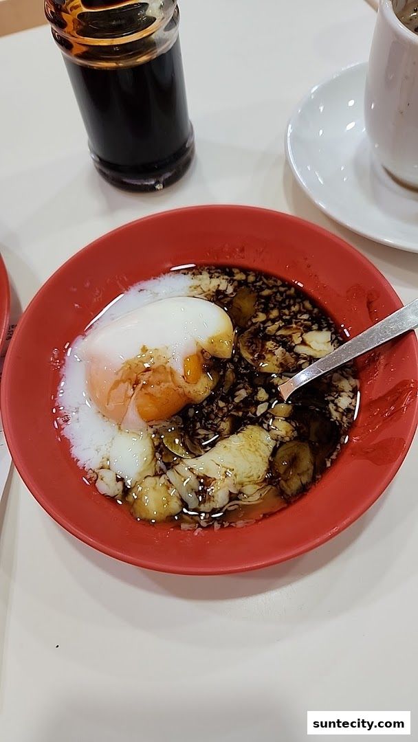 A close-up of a red bowl filled with soft-boiled eggs and soy sauce, with a bottle of soy sauce and a cup in the background.
