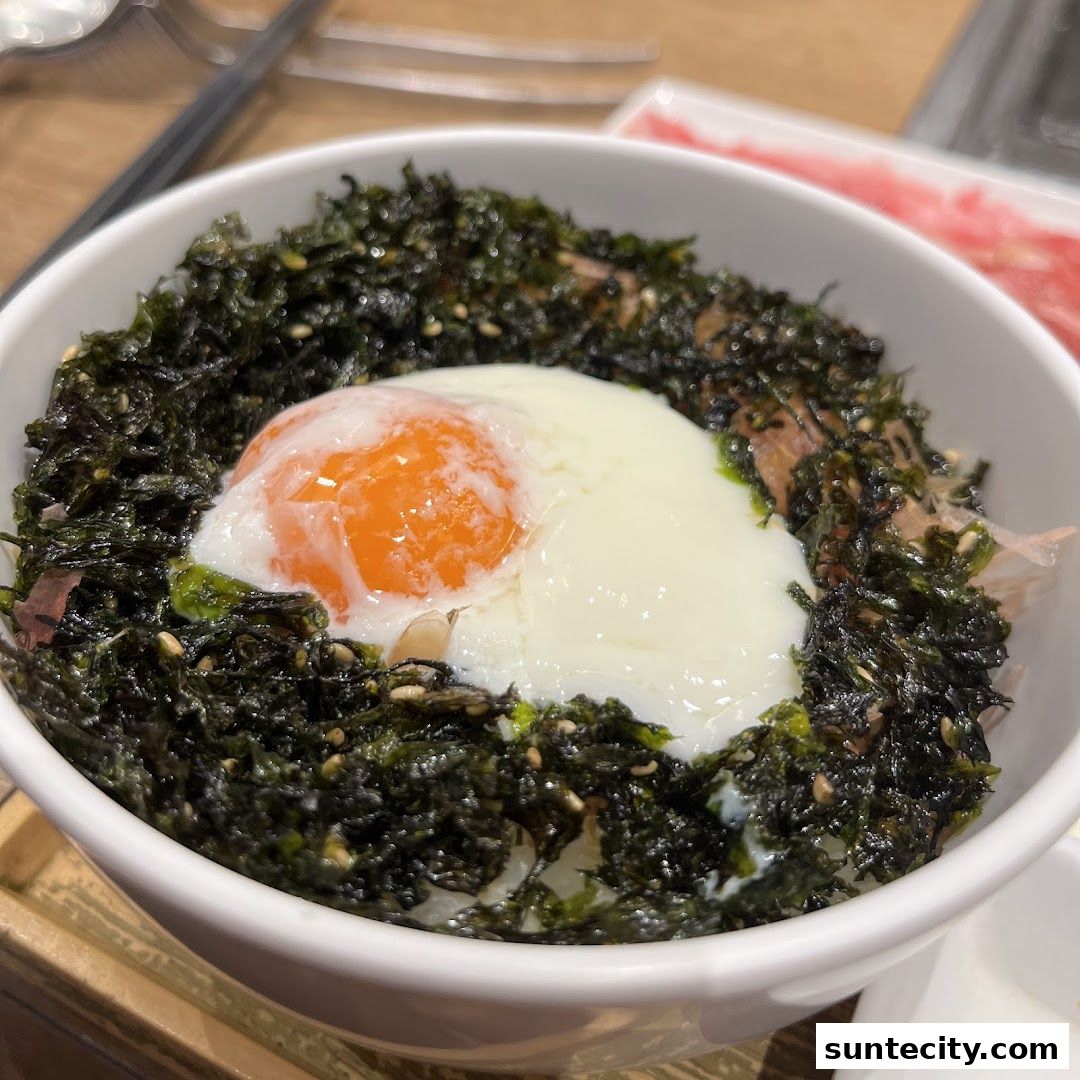 A close-up of a bowl of rice topped with seaweed, a soft-boiled egg, and meat.