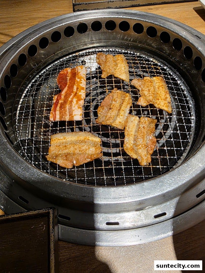 Sizzling pork belly grilling on a circular barbecue grill at Yakiniku Like.