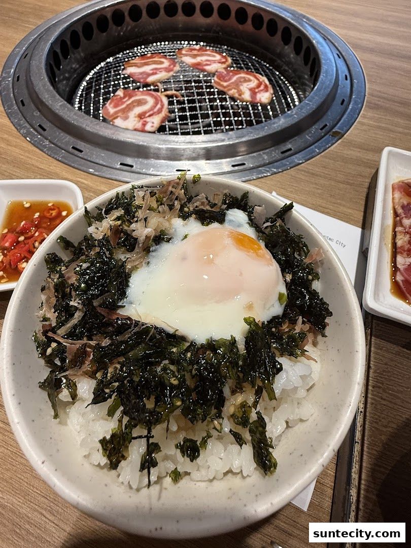 A bowl of rice topped with seaweed and a soft-boiled egg, with grilled meat in the background.