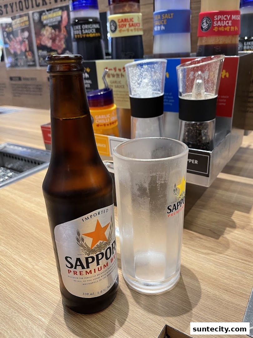 A bottle of Sapporo Premium Beer and a frosted glass on a wooden table with various sauces in the background.