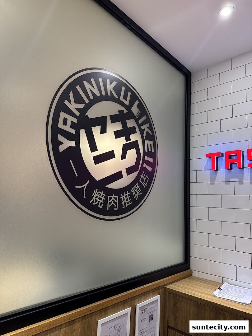 The Yakiniku Like logo is displayed on a frosted glass window with a brick wall and neon sign in the background.