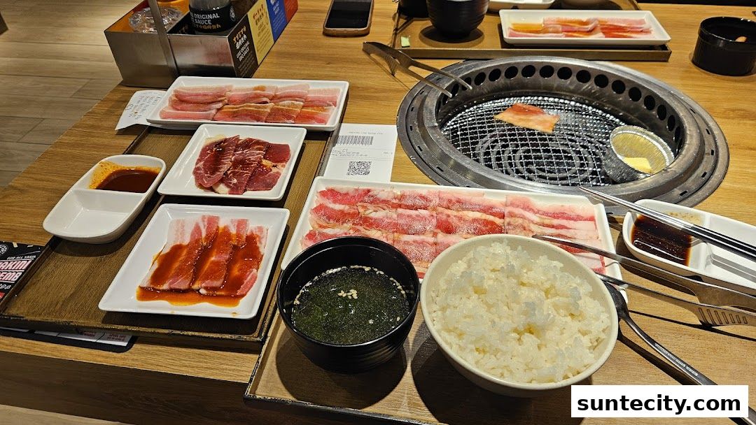 A table set for yakiniku with various cuts of meat, rice, soup, and dipping sauces.