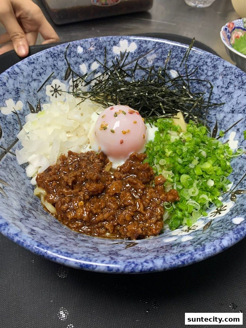 A bowl of Japanese noodles with minced meat, egg, seaweed, and green onions.