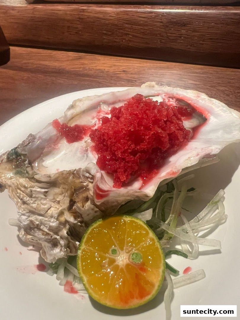 A single oyster served with a citrus slice and shredded vegetables on a white plate.